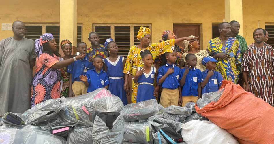 Image is of a group of children receiving sacks of back packs and supplies